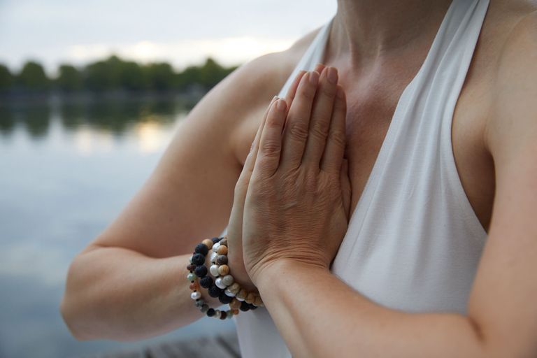 Frau in weißem Trägertop mit Händen in Gebetshaltung vor der Brust vor See als Hintergrund Kundalini Yoga Meditation und Entspannung in Hannover