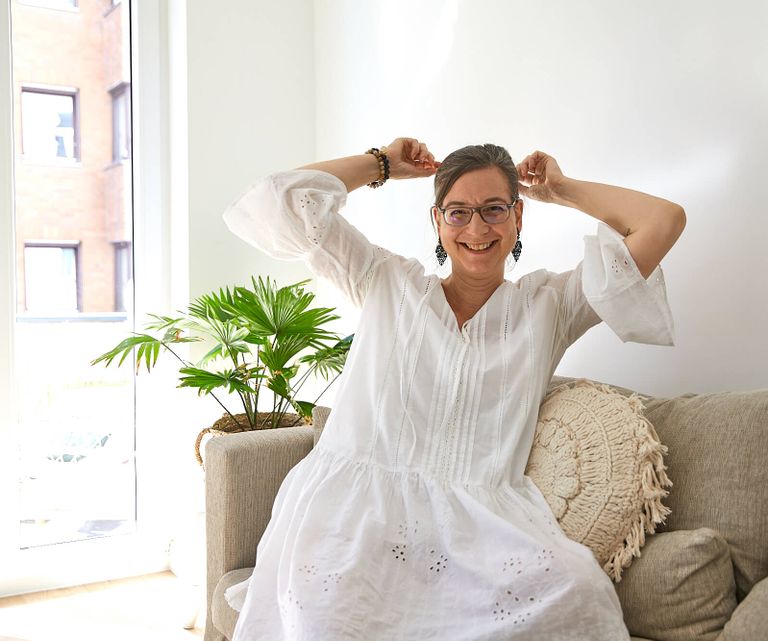 Portrait Prem Jaijeet Kaur von Kundalini Yoga Mediation und Entspannung in Hannover - auf Sofa sitzend in weißem Kleid mit Grünpflanze im Hintergrund