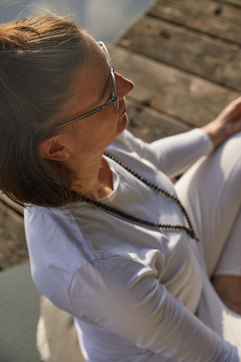 Frau in weißer Kleidung mit mittellangen Haaren Brille und Mala-Kette in Meditationshaltung von oben fotografiert, Kundalini Yoga Meditation und Entspannung in Hannover Maschsee Yoga im Park