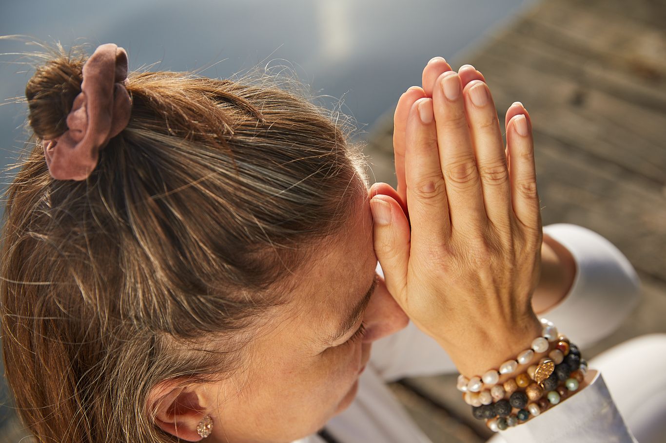 Kundalini Yoga Meditation Entspannung Workshop Bliss Hannover Ausschnittbild von Frauenarmen in weißen Ärmeln mit Perlenarmbändern und Here and Now Tattoo