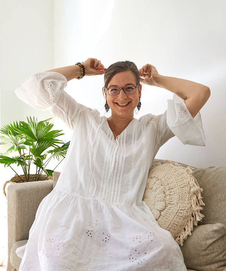 Portrait Prem Jaijeet Kaur von Kundalini Yoga Mediation und Entspannung in Hannover - auf Sofa sitzend in weißem Kleid mit Grünpflanze im Hintergrund
